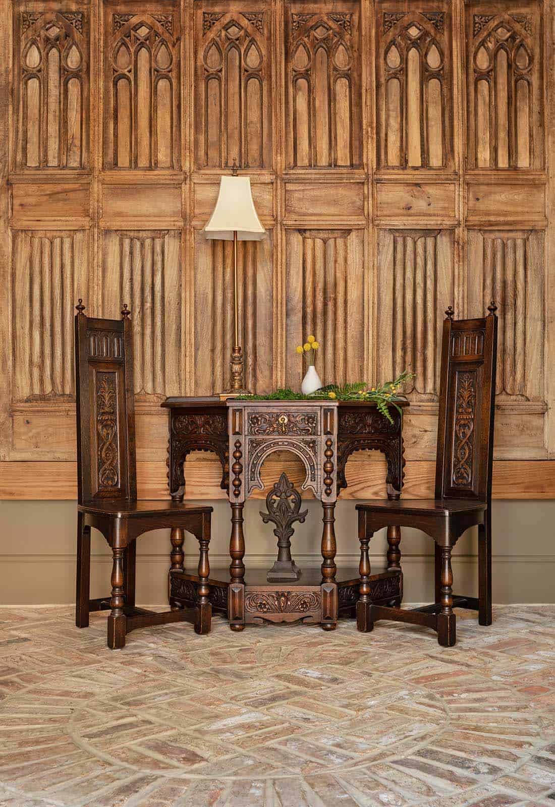 Gothic carved wood wall panels with antique oak high-back chairs and ornate carved console table