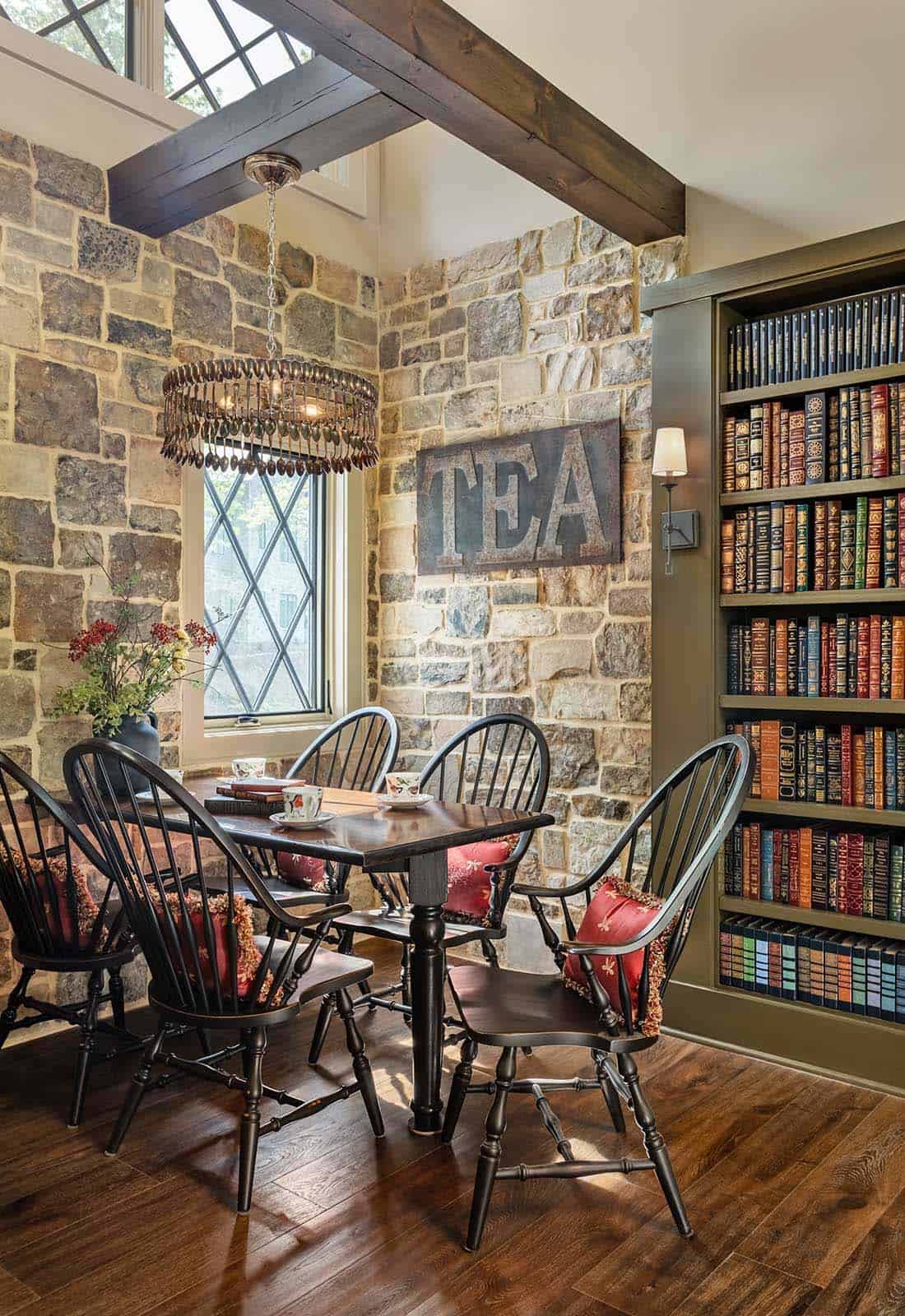 Cozy tea room with stone walls, Windsor chairs, diamond-pane window, and floor-to-ceiling bookshelf