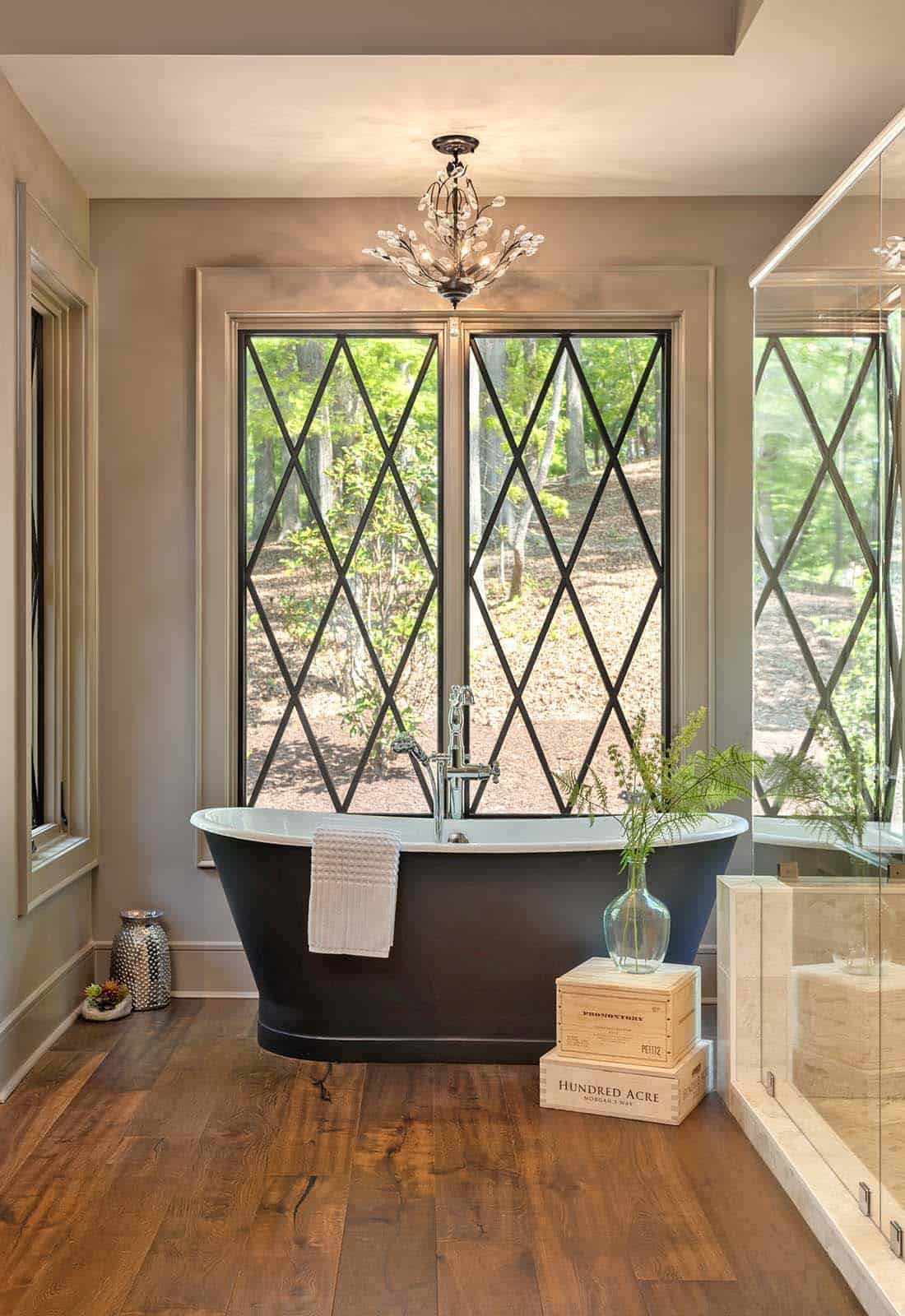 Freestanding soaking tub centered before large diamond-pane windows overlooking wooded landscape
