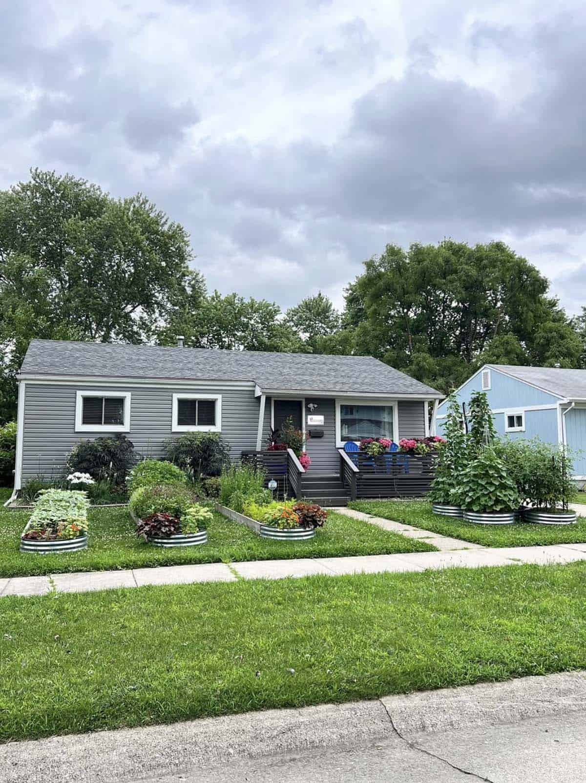 Front yard with galvanized circle and rectangle raised beds planted with vegetables, flowers and climbing beans in front of a gray ranch home