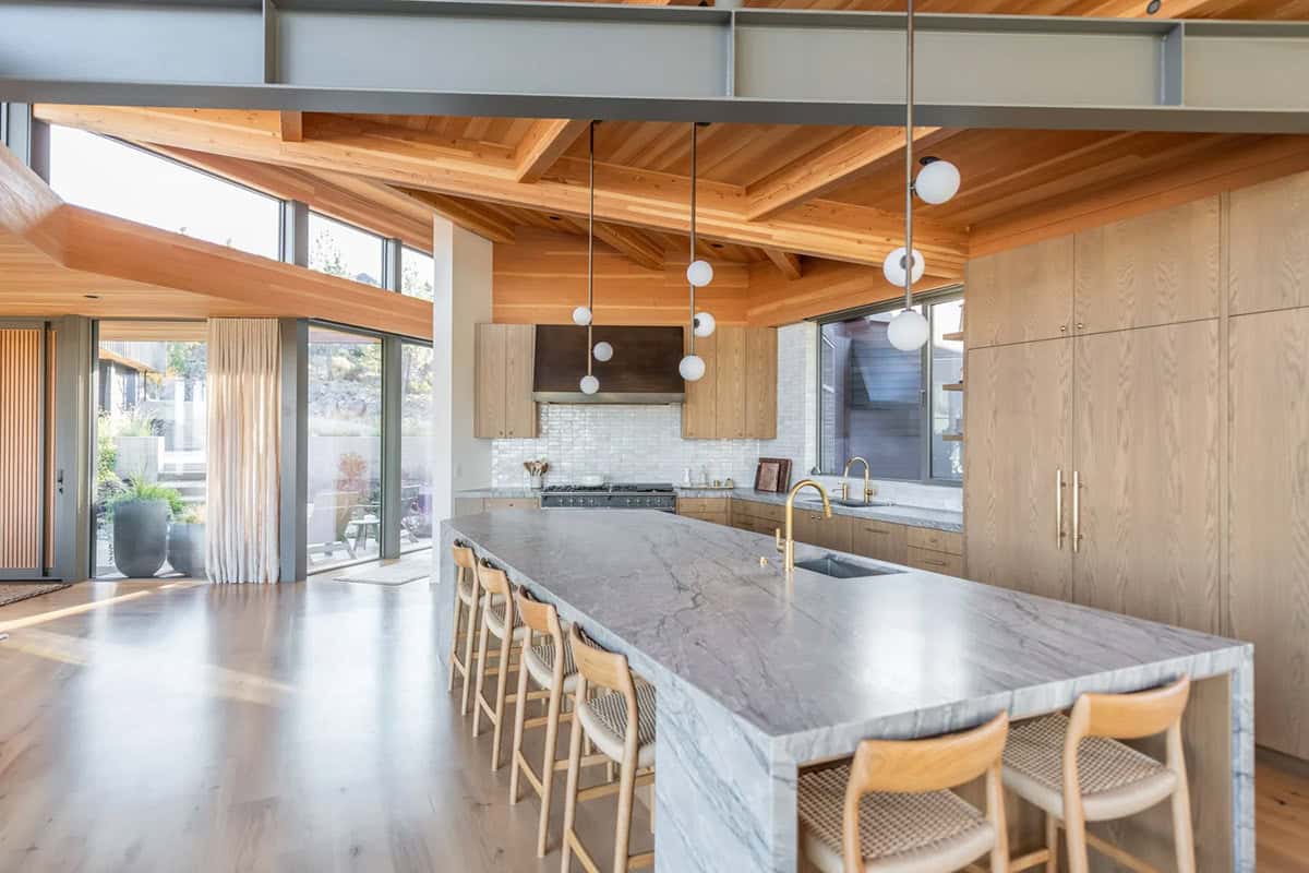 Large marble kitchen island with globe pendant lights and exposed wood beam ceiling
