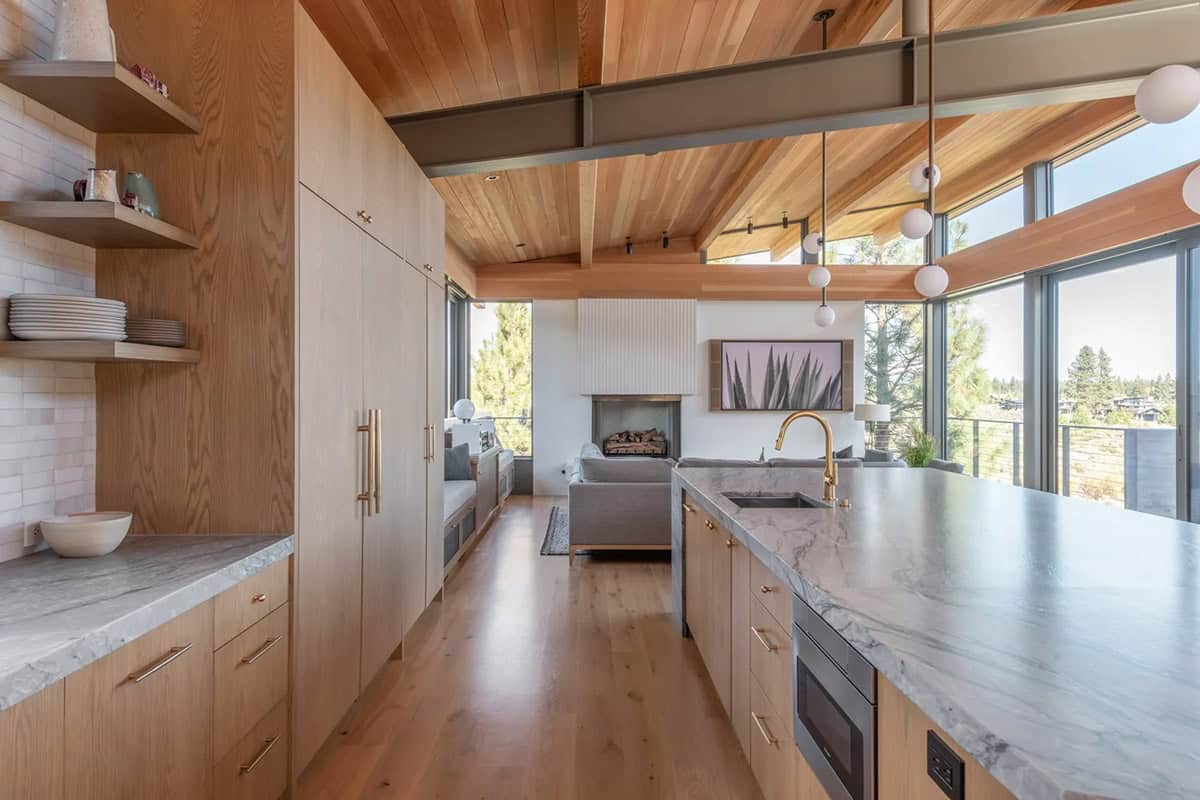 White oak kitchen with marble countertops and open shelving leading to living room