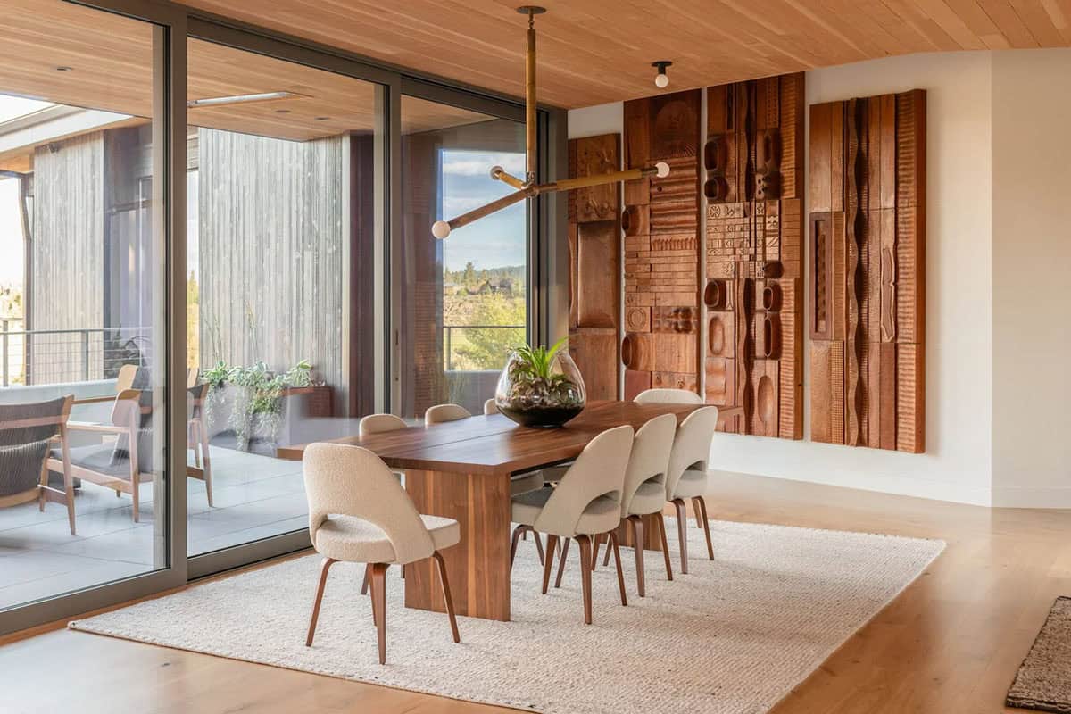 Walnut dining table with carved wood wall art and sliding glass doors to terrace
