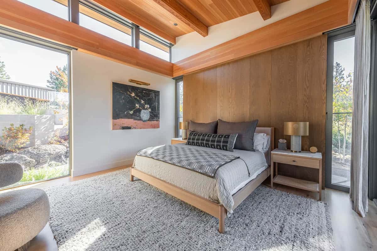 Primary bedroom with wood-paneled accent wall, clerestory windows, and garden views