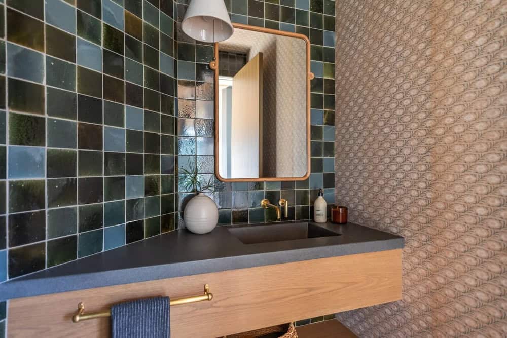Powder room with deep teal zellige tile, brass fixtures, and textured wallpaper