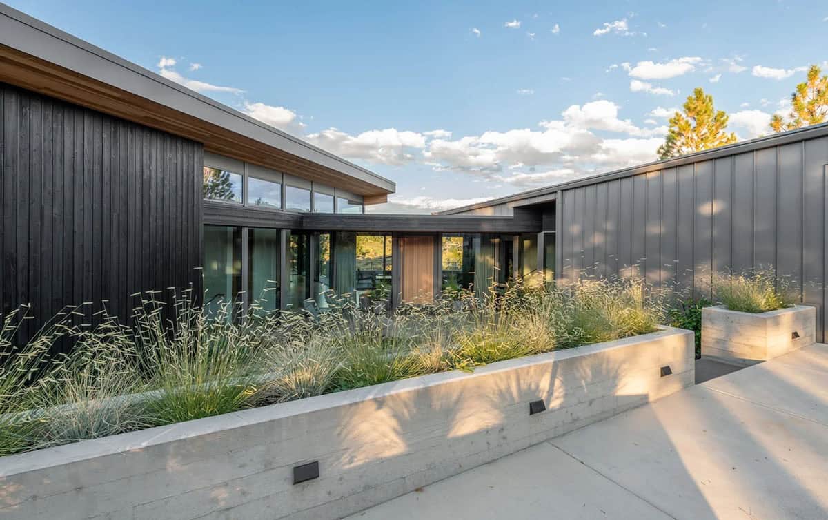 Home entry with dark vertical siding, concrete planters with feather reed grass