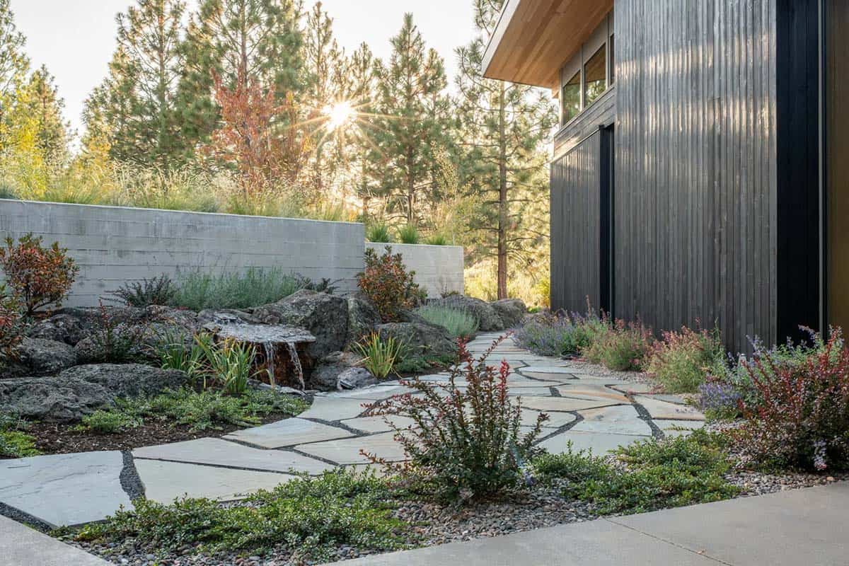 Flagstone path with water feature and drought-tolerant plantings beside dark wood siding
