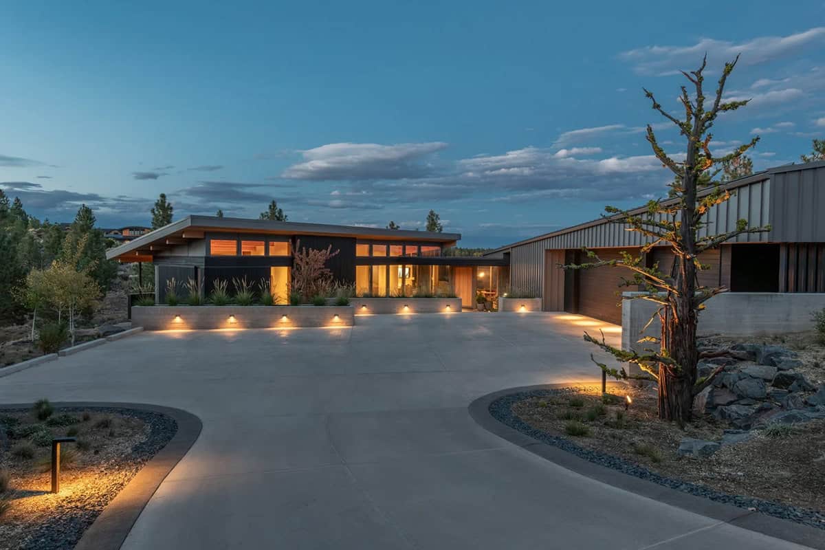 Modern high desert home exterior lit up at dusk with concrete planters and ponderosa pine trees