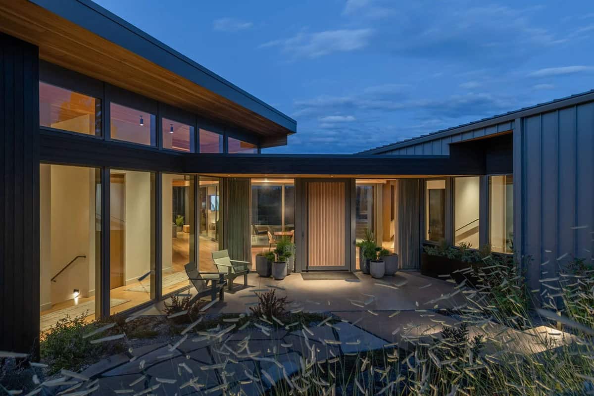 Illuminated front entry courtyard at dusk with slatted wood door and floor-to-ceiling glazing