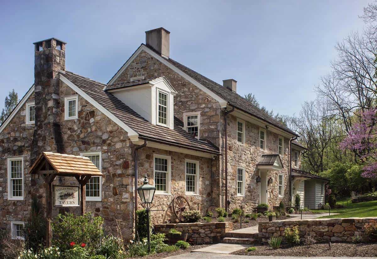 Stone farmhouse with cedar shake roof, two chimneys, and Valley Springs Tavern sign in front yard