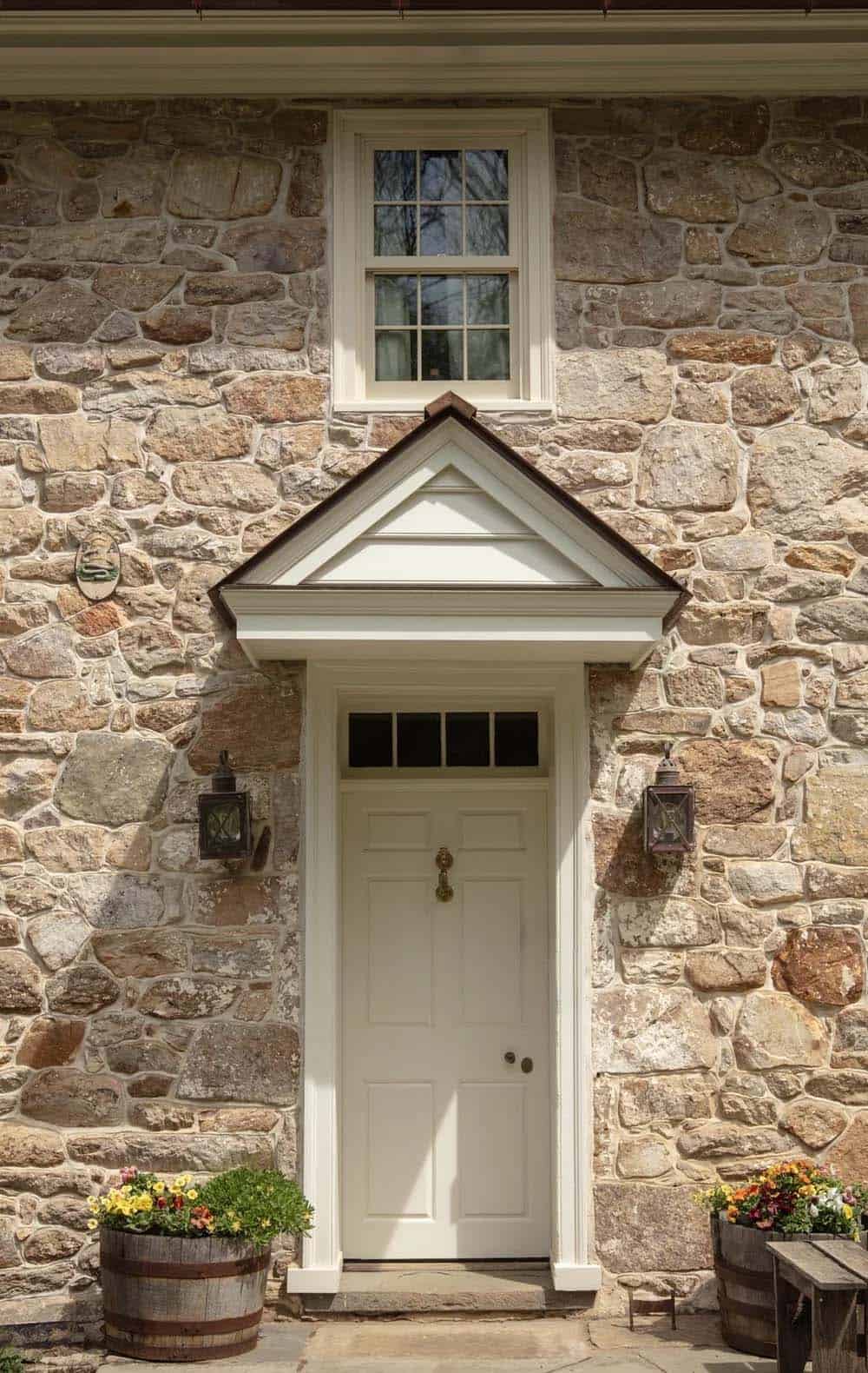 Front door with pedimented hood, flanking lanterns, and flower-filled barrel planters