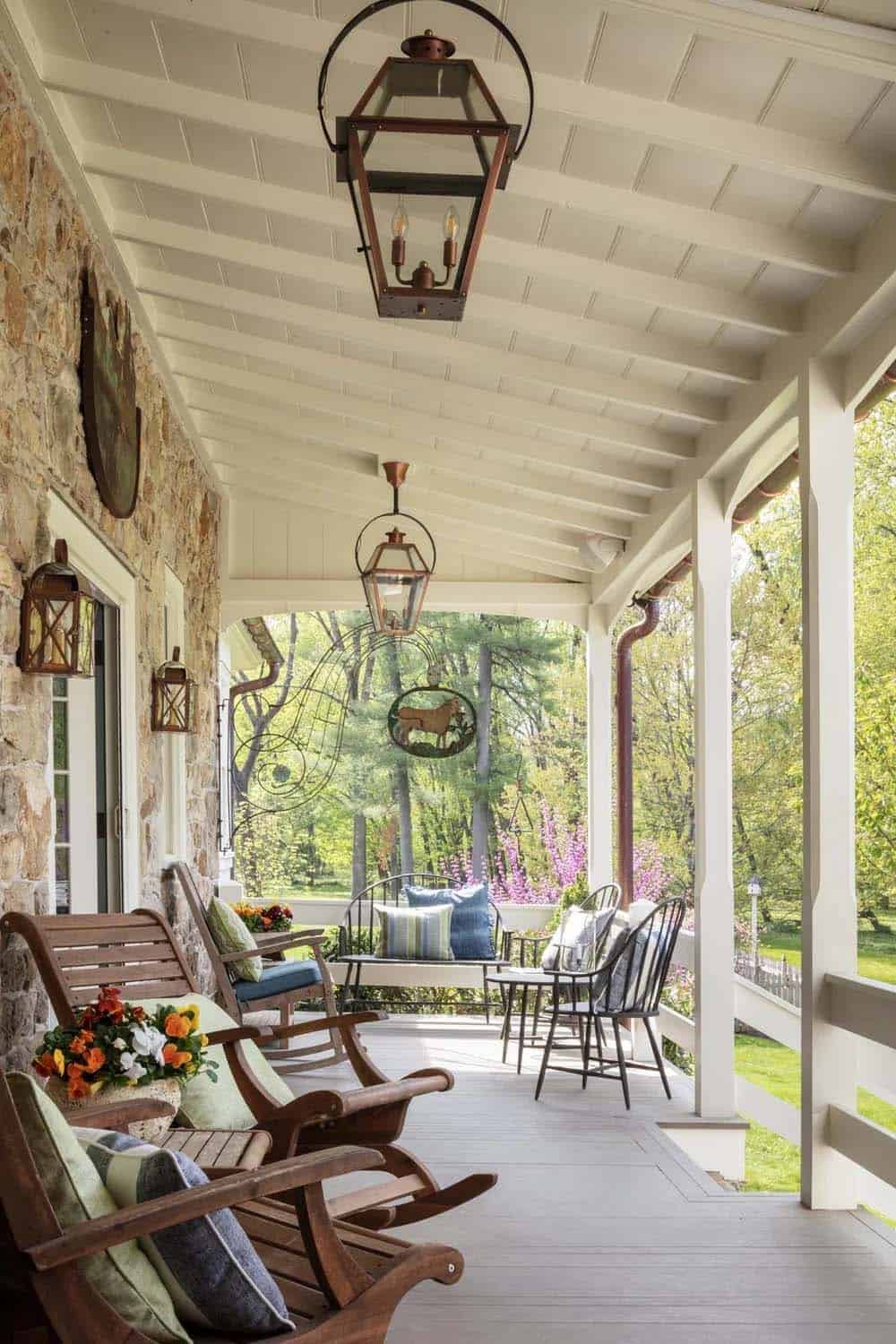 Covered porch with copper lanterns, rocking chairs, and view of garden and redbud trees