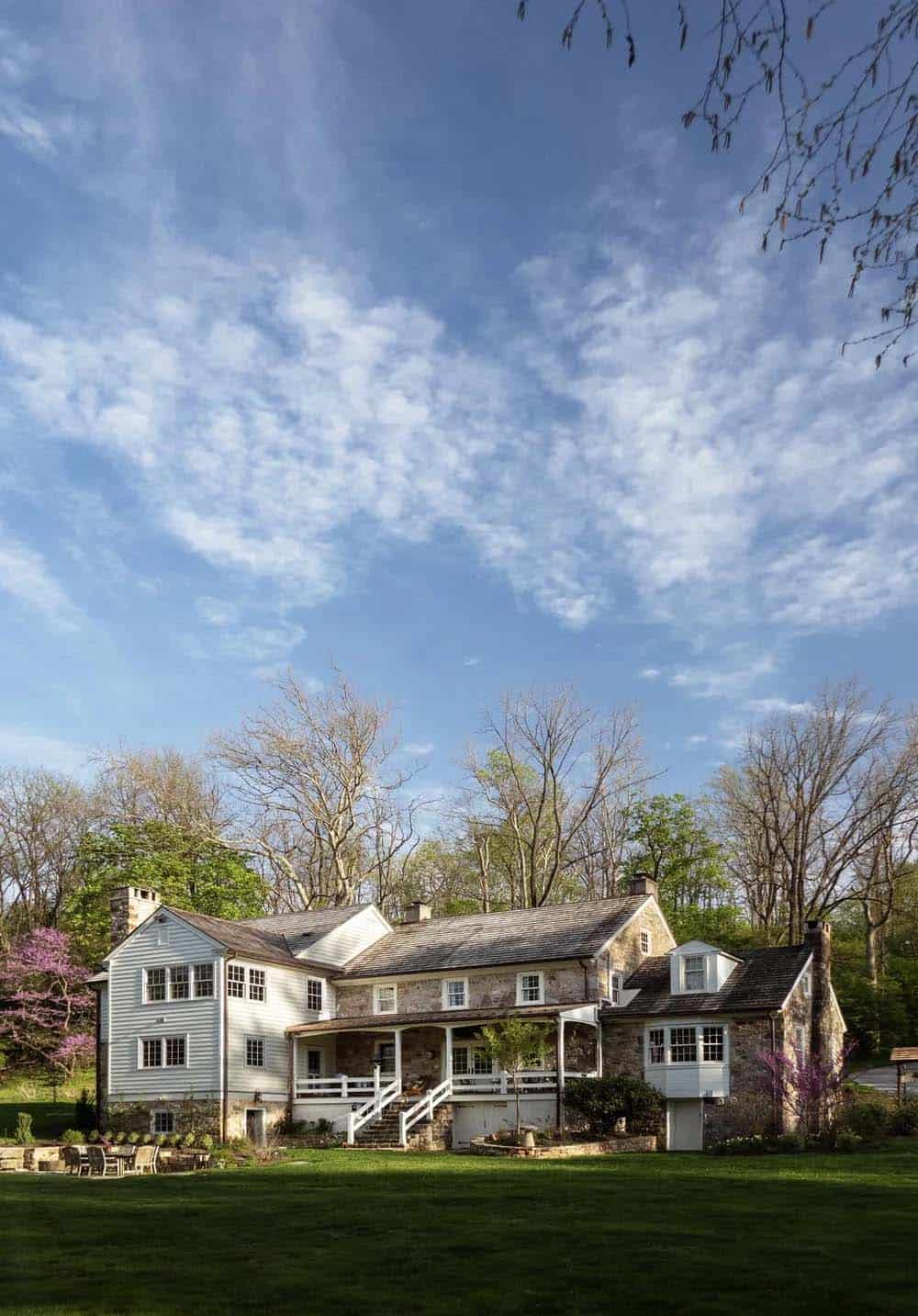 Rear view of stone-and-clapboard home under a wide blue sky with sweeping lawn