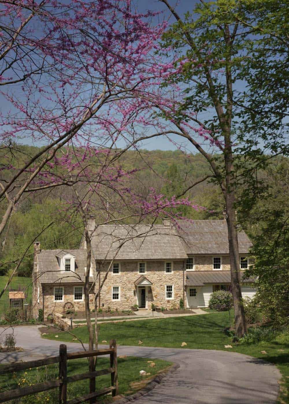 Stone farmhouse viewed through blooming redbud branches along the driveway