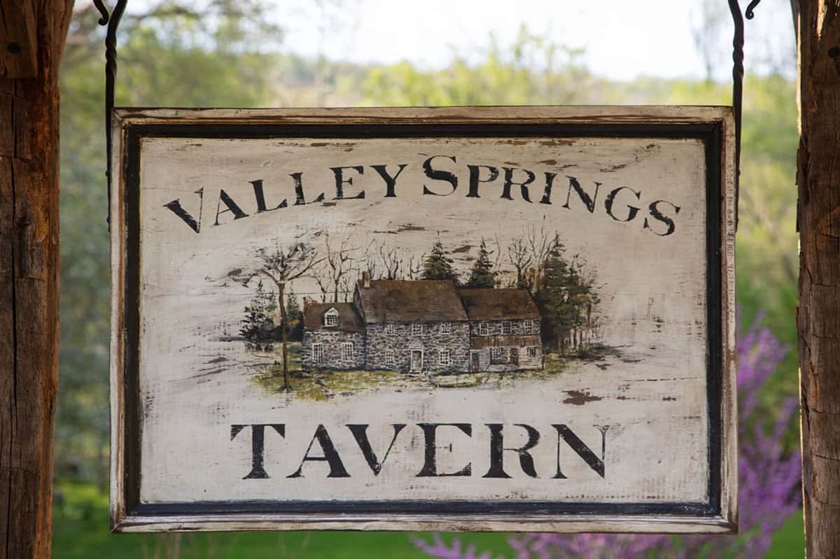 Hand-painted "Valley Springs Tavern" sign depicting the stone house, framed by greenery