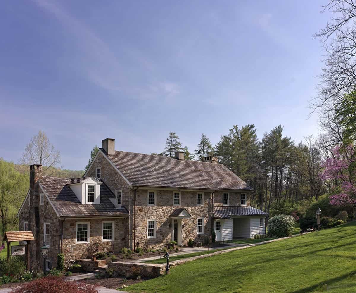 Wide exterior view of the stone farmhouse and grounds under a clear blue sky