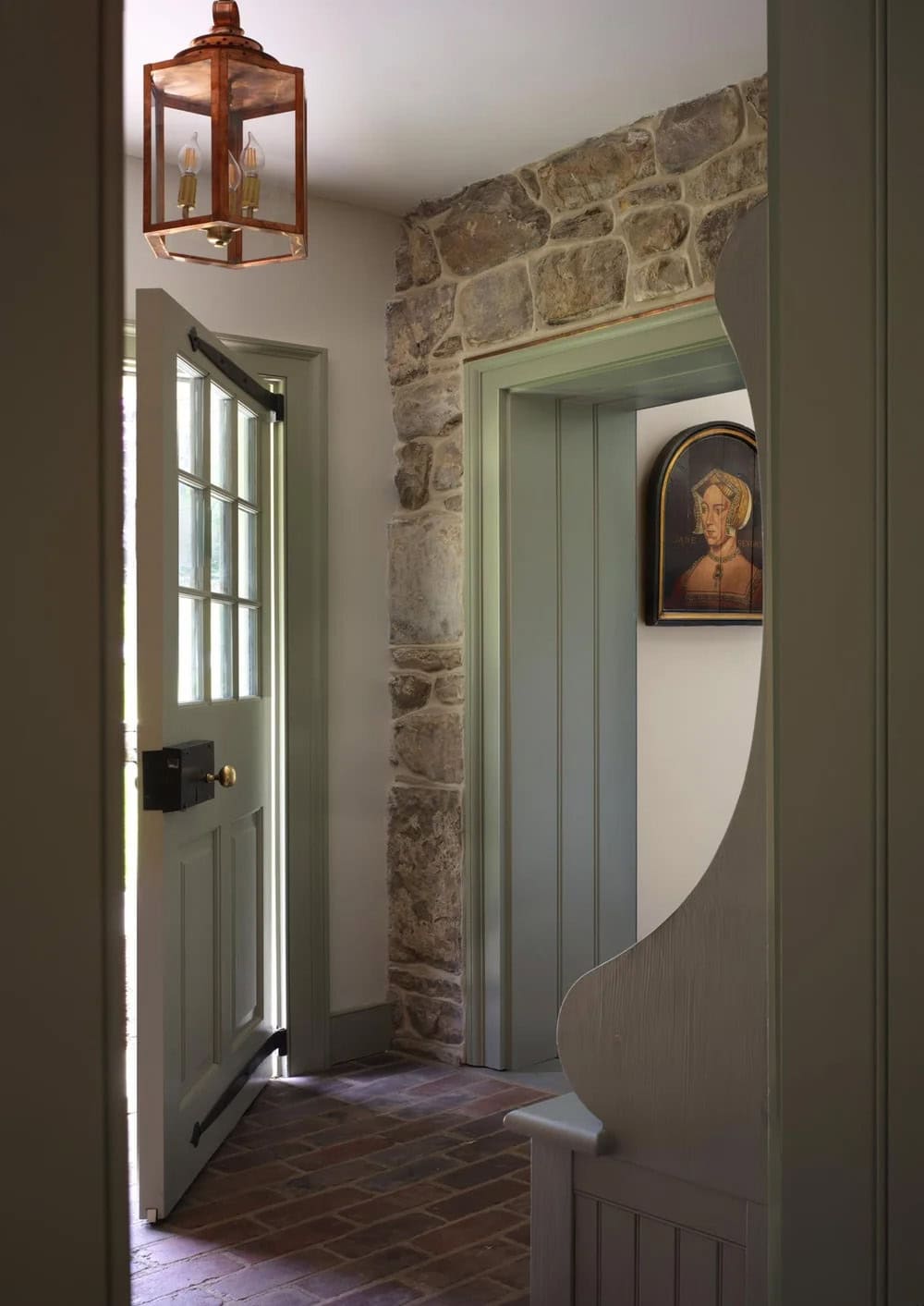 Entryway with stone wall, copper lantern, and Tudor portrait visible through doorway