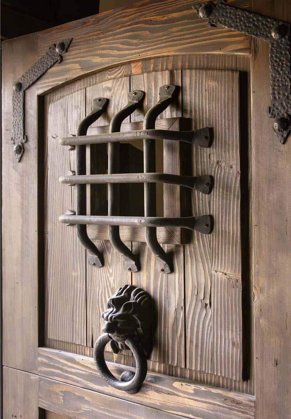 Detail of rustic wood door with iron grille window and lion's head ring knocker