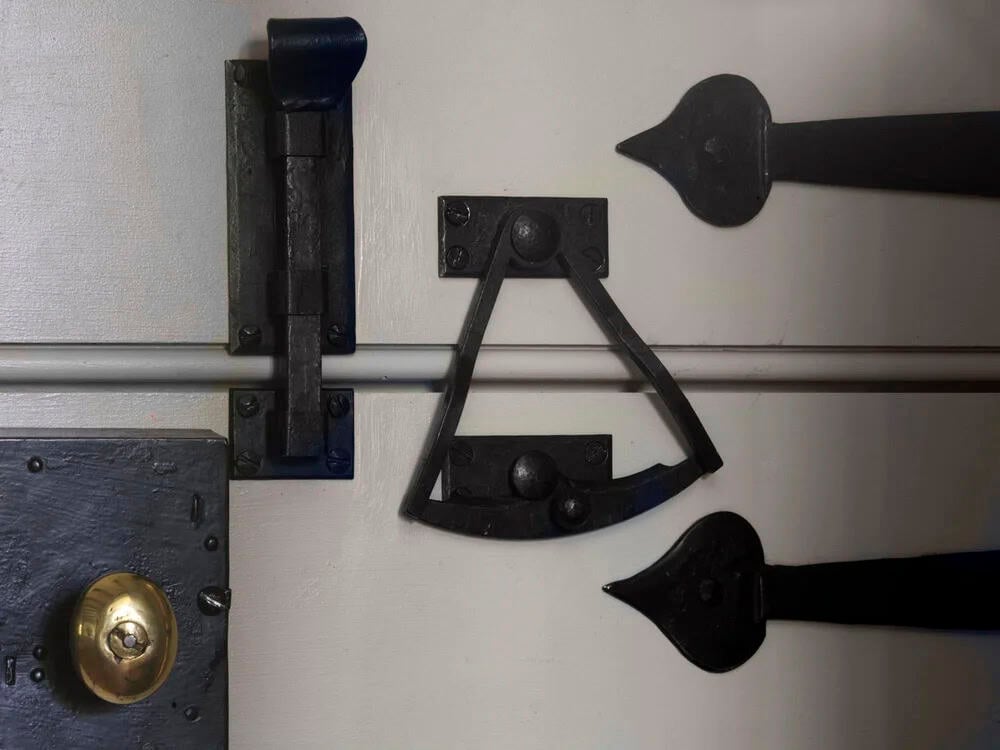 Detail of black iron door hardware including latch, knob, and decorative hinge straps