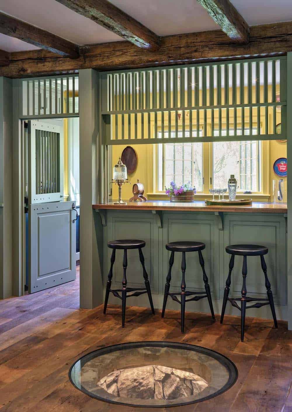 Sage-green home bar with slatted divider, yellow walls, and stocked liquor shelves