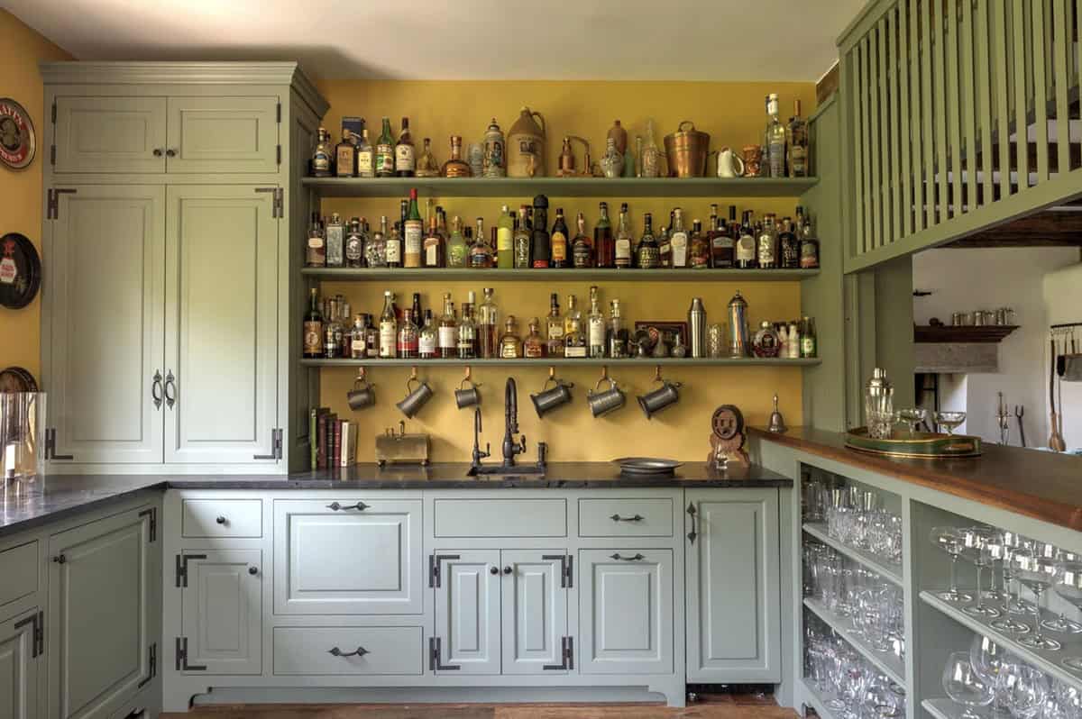 Wide view of green-paneled bar area with shelved spirits and hanging pewter mugs