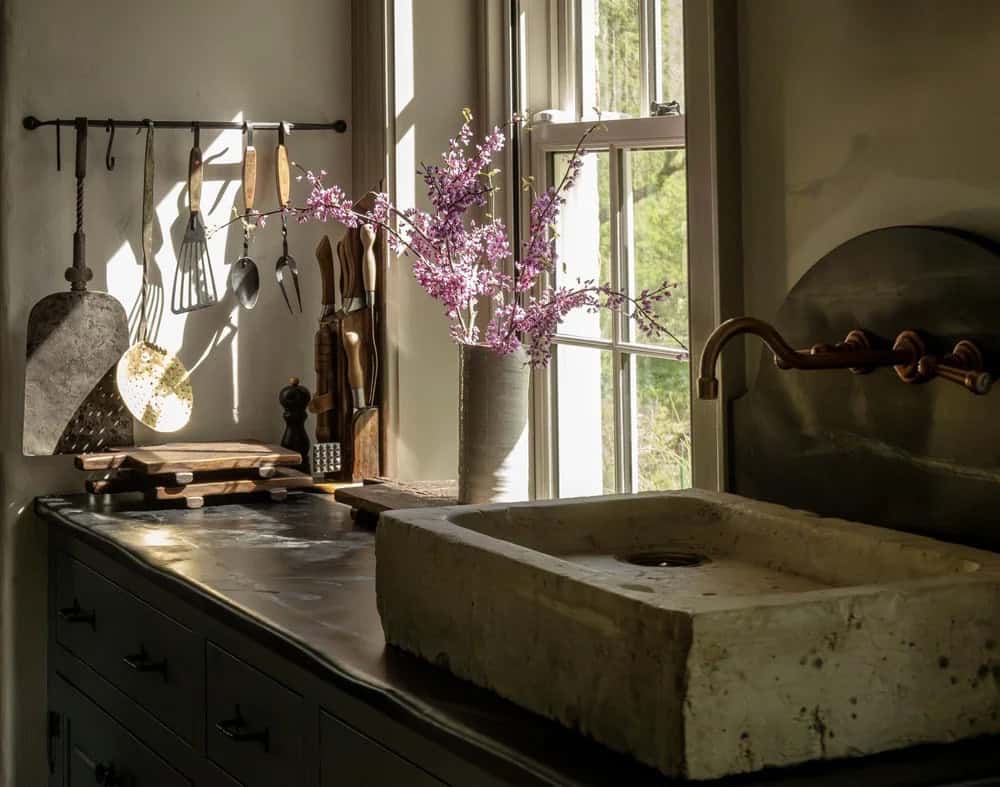 Kitchen counter with carved stone sink, hanging utensils, and flowering branch