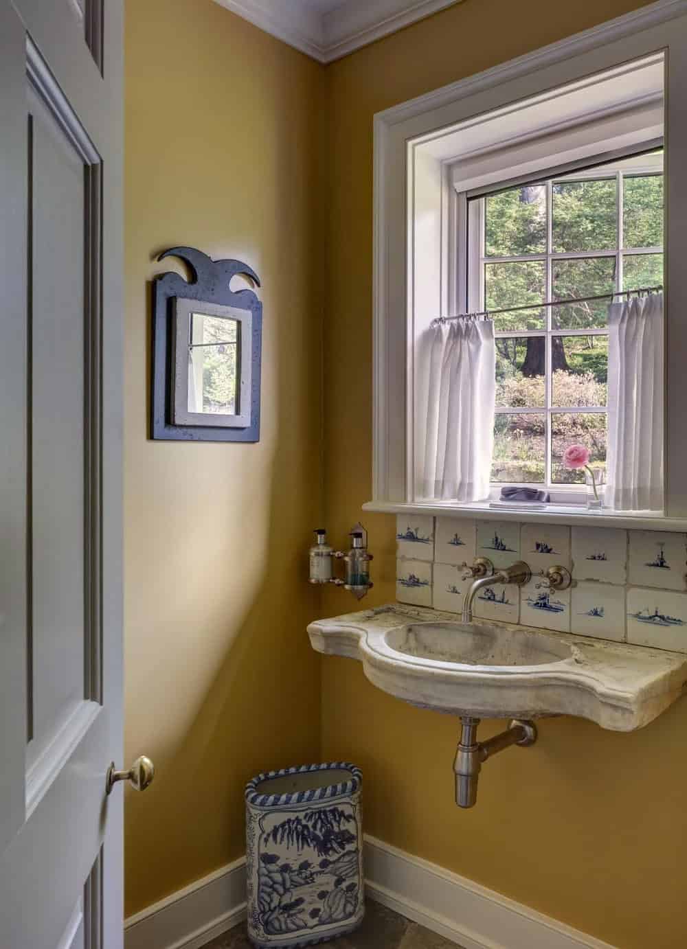 Mustard-yellow powder room with carved stone sink and Delft-style tile backsplash