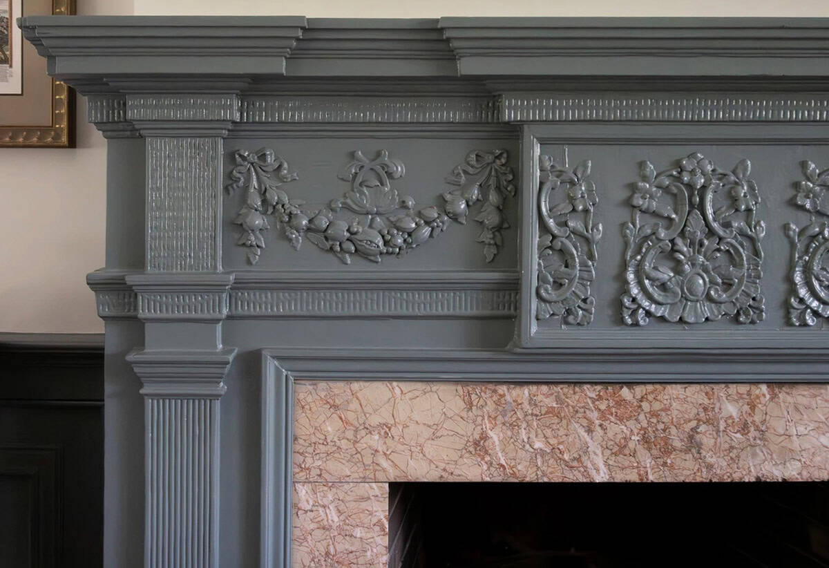 Close-up of carved gray fireplace mantel with floral swag and rosette details above marble surround