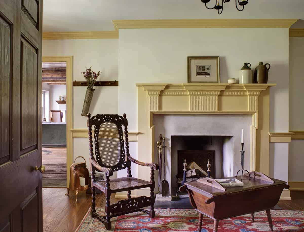 Sitting room with yellow-trimmed fireplace, antique caned armchair, and patterned rug