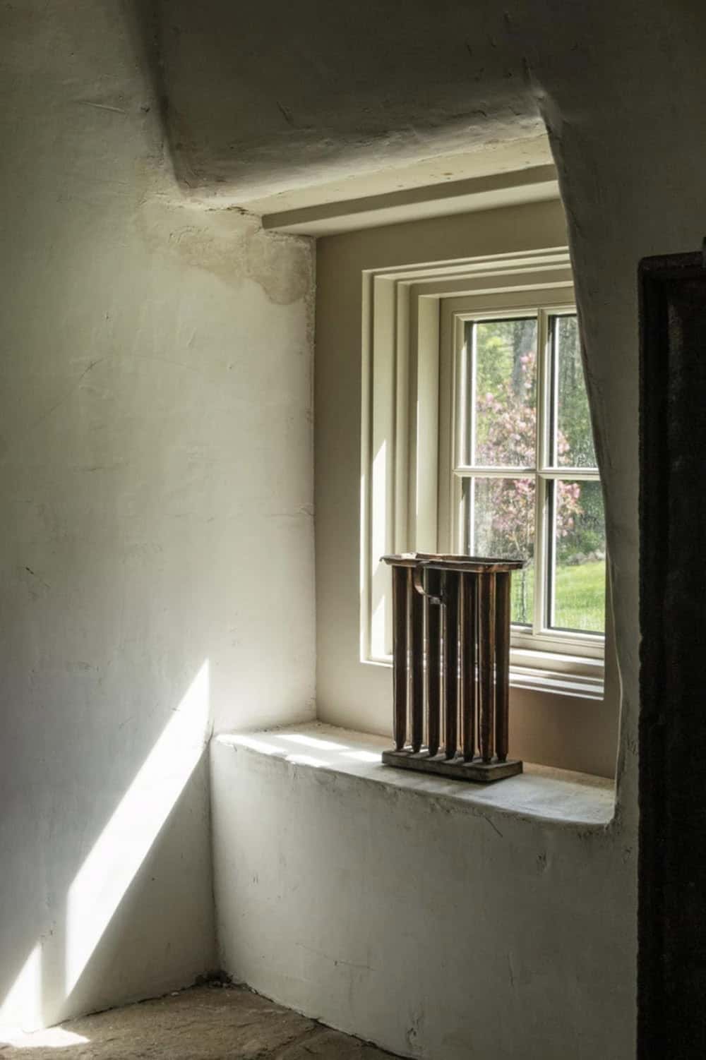 Sunlit window nook with deep plaster sill and sculptural wood candle holder