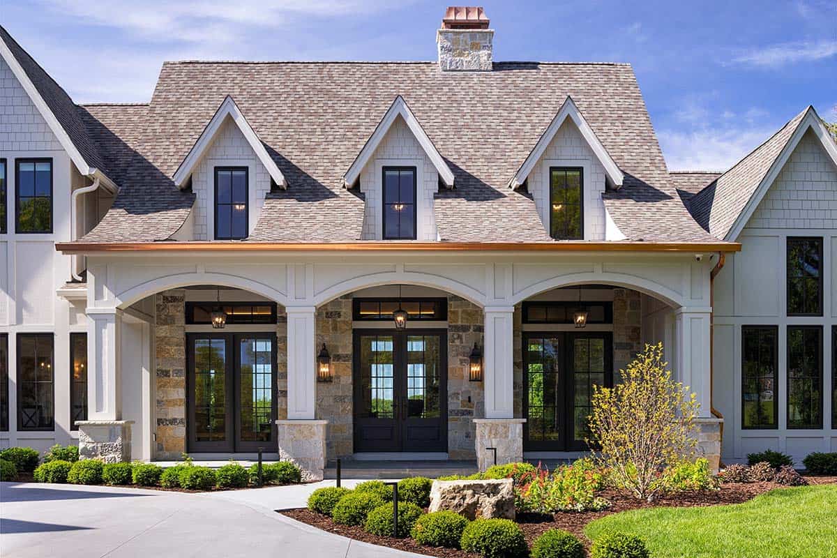 Arched stone entry porch with three sets of glass French doors and copper gutter trim