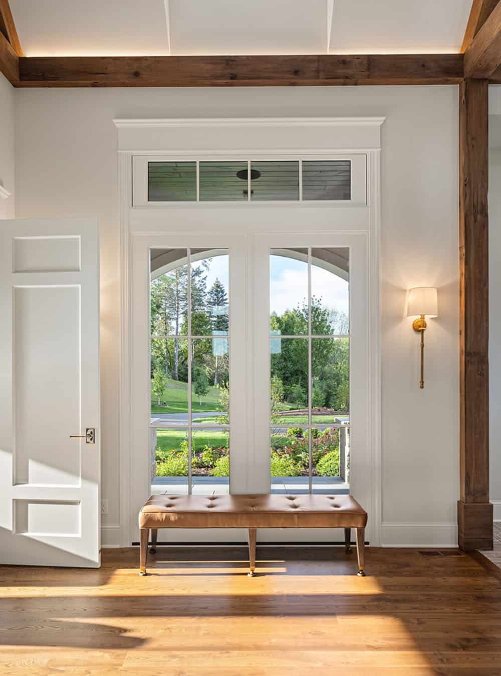 Foyer with arched French doors, leather bench, and exposed wood ceiling beams
