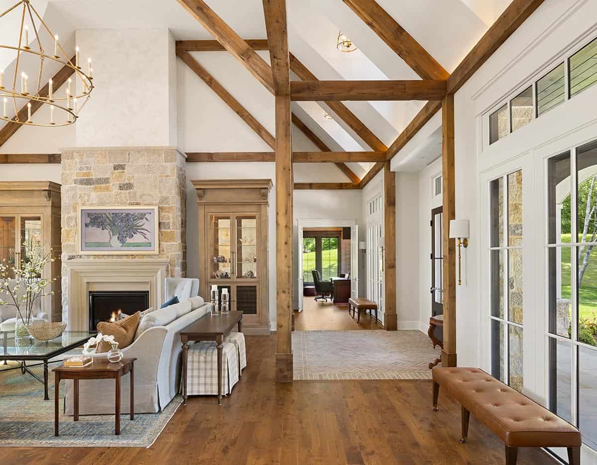 Living area with stone fireplace, exposed beams, and view into home office