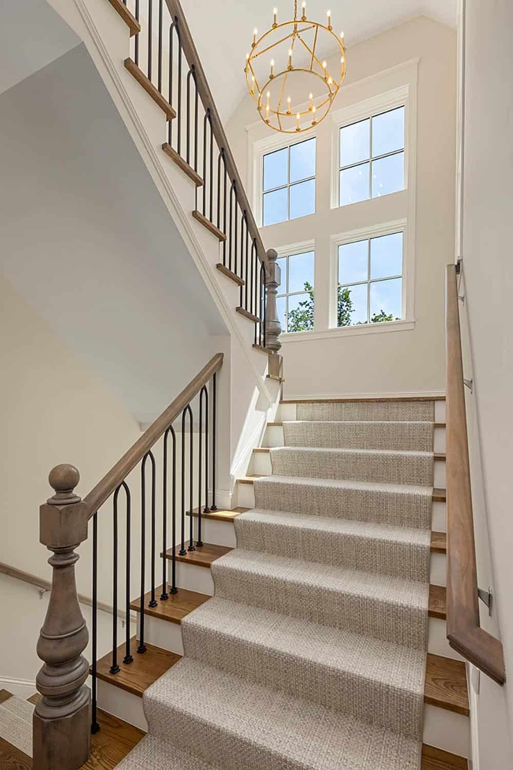 Staircase with wrought-iron balusters, wood railing, and round chandelier