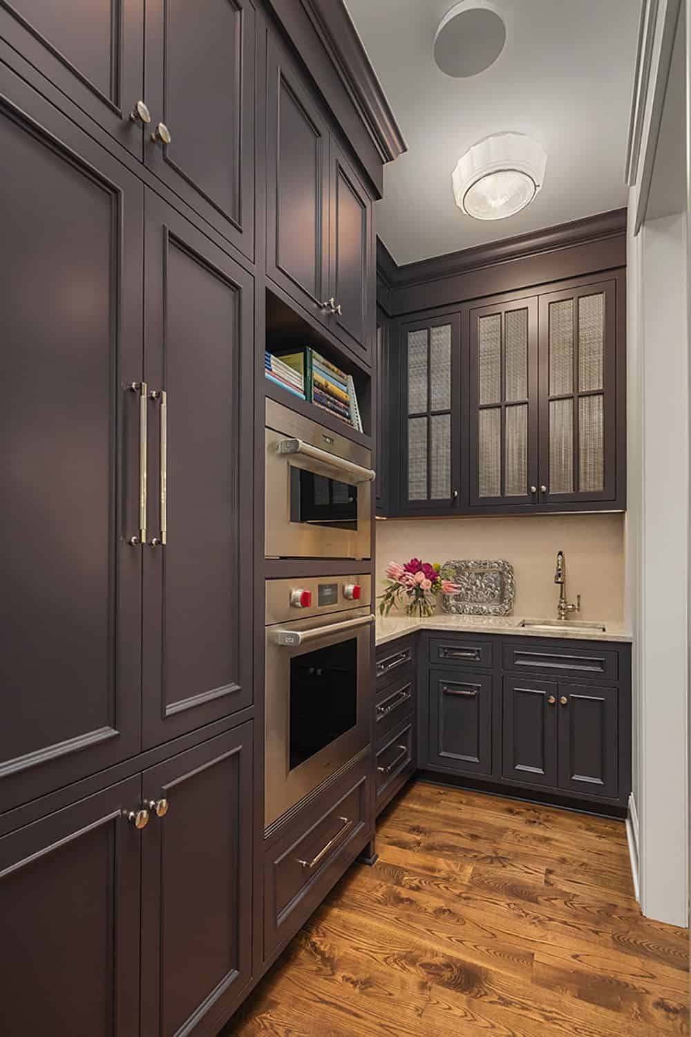 Butler's pantry with dark cabinetry, built-in ovens, and glass-front uppers
