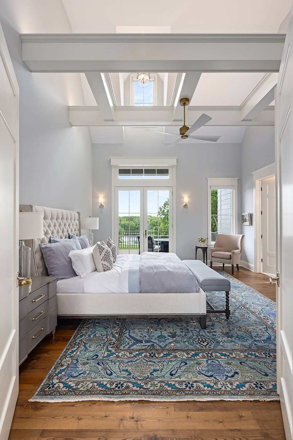 Primary bedroom with tufted headboard, beamed ceiling, and blue patterned rug
