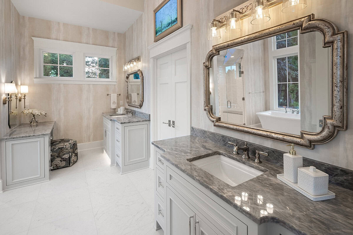 Primary bathroom with marble flooring, freestanding tub reflection, and seating area