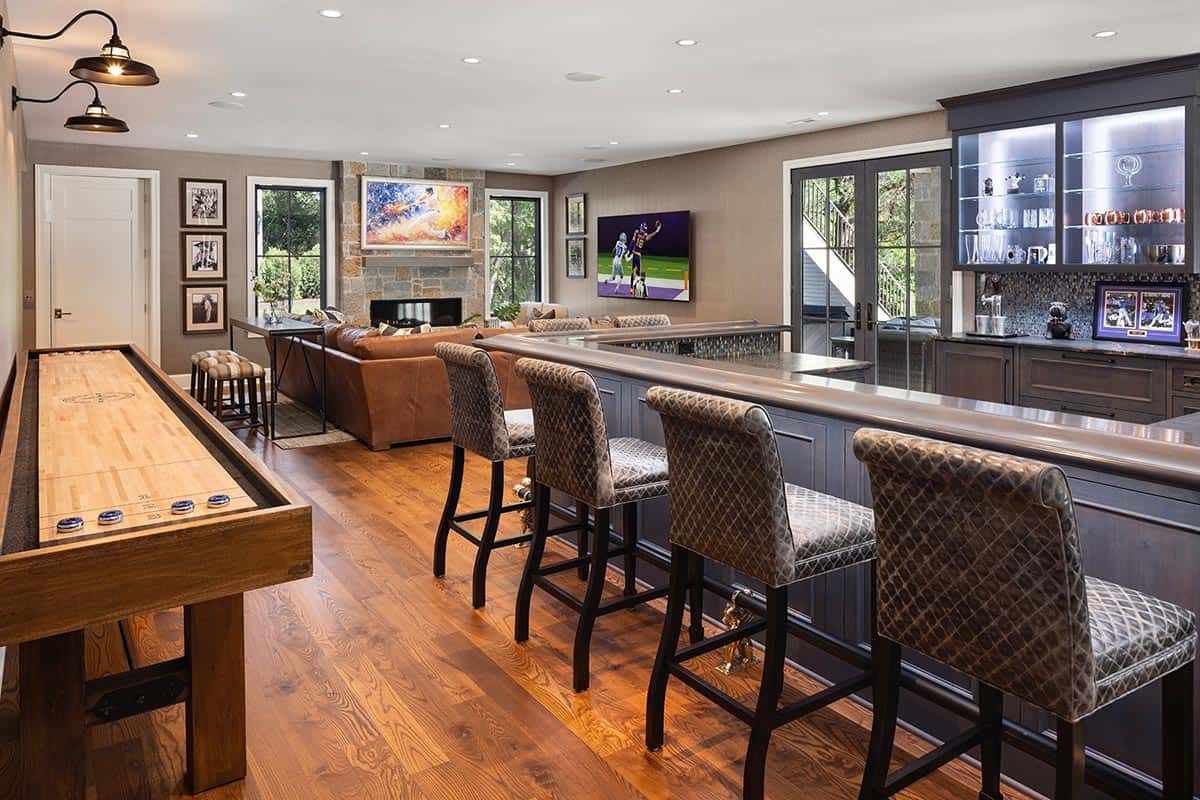 Basement lounge with shuffleboard table, leather sofa, and stone fireplace