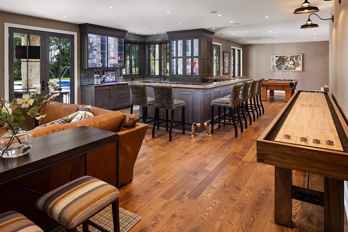 Basement bar with dark cabinetry, glass display shelves, and patterned barstools