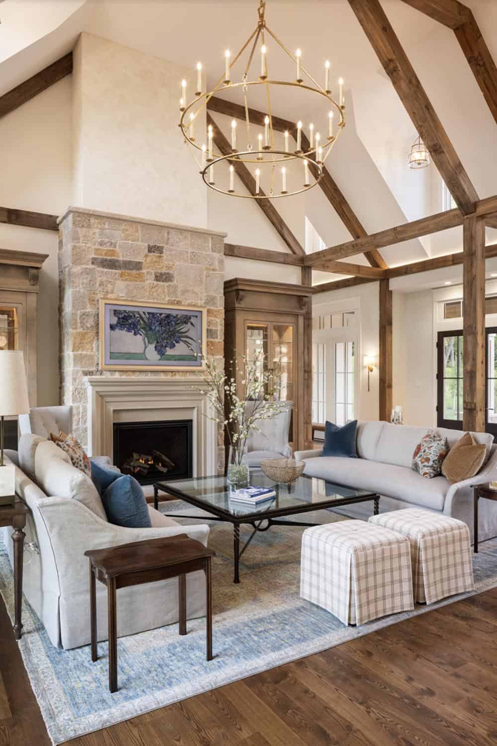 Living room with two-story stone fireplace, beamed ceiling, and tiered brass chandelier
