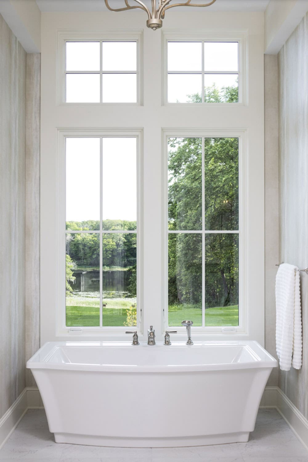 Freestanding soaking tub beneath tall windows overlooking the lake