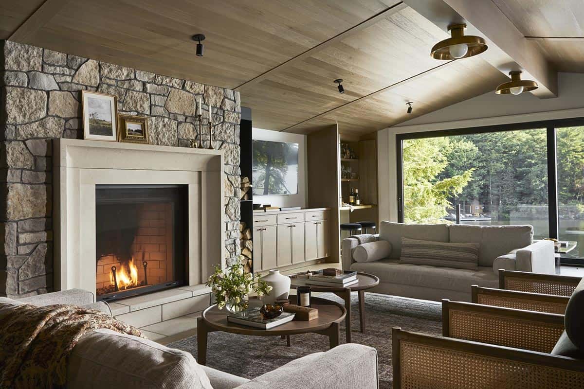 Living room with fieldstone fireplace, wood-clad vaulted ceiling, and lake view through floor-to-ceiling windows