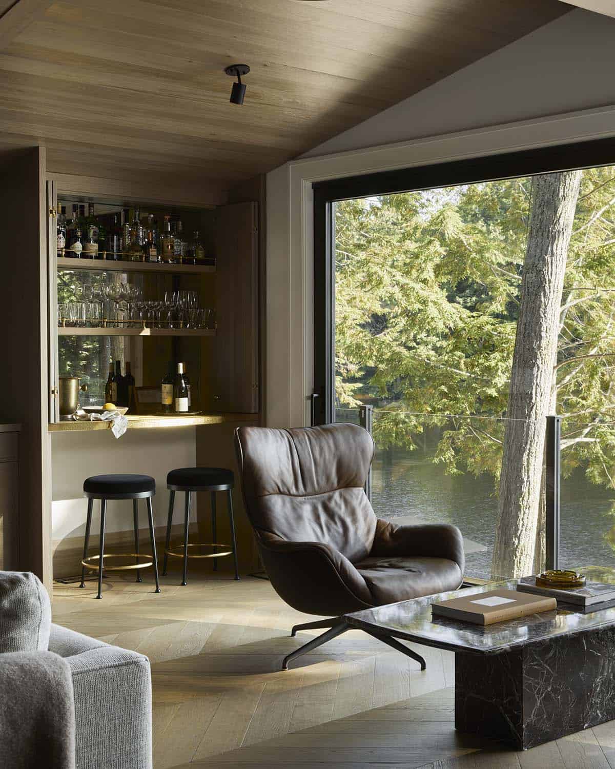 Reading nook with leather lounge chair, open bar cabinet, and forest view window