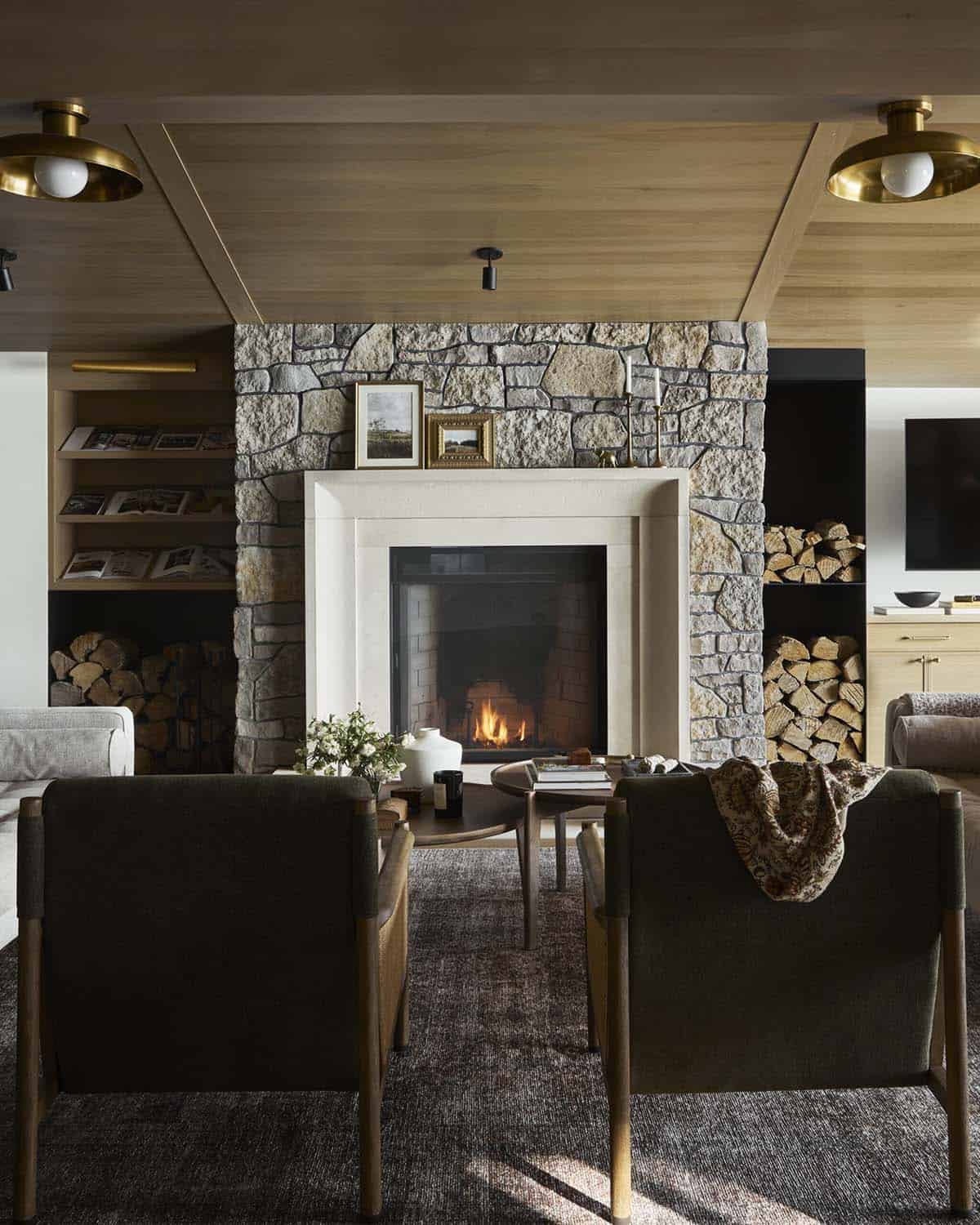 Two dark lounge chairs facing a stone fireplace with built-in log storage and bookshelves