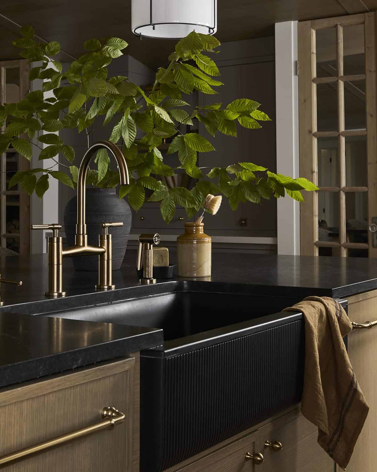 Kitchen sink detail with brass gooseneck faucet, black farmhouse sink, and greenery