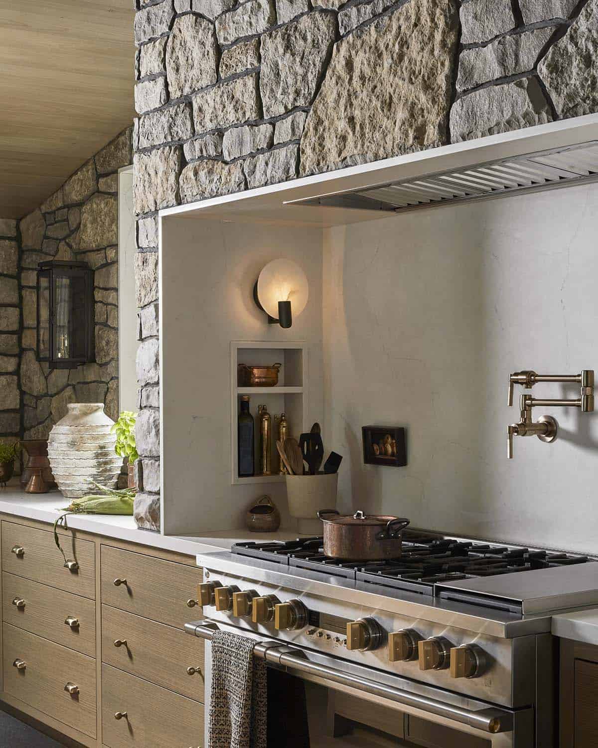 Kitchen range nook with stone hood surround, brass pot filler, and wall sconce