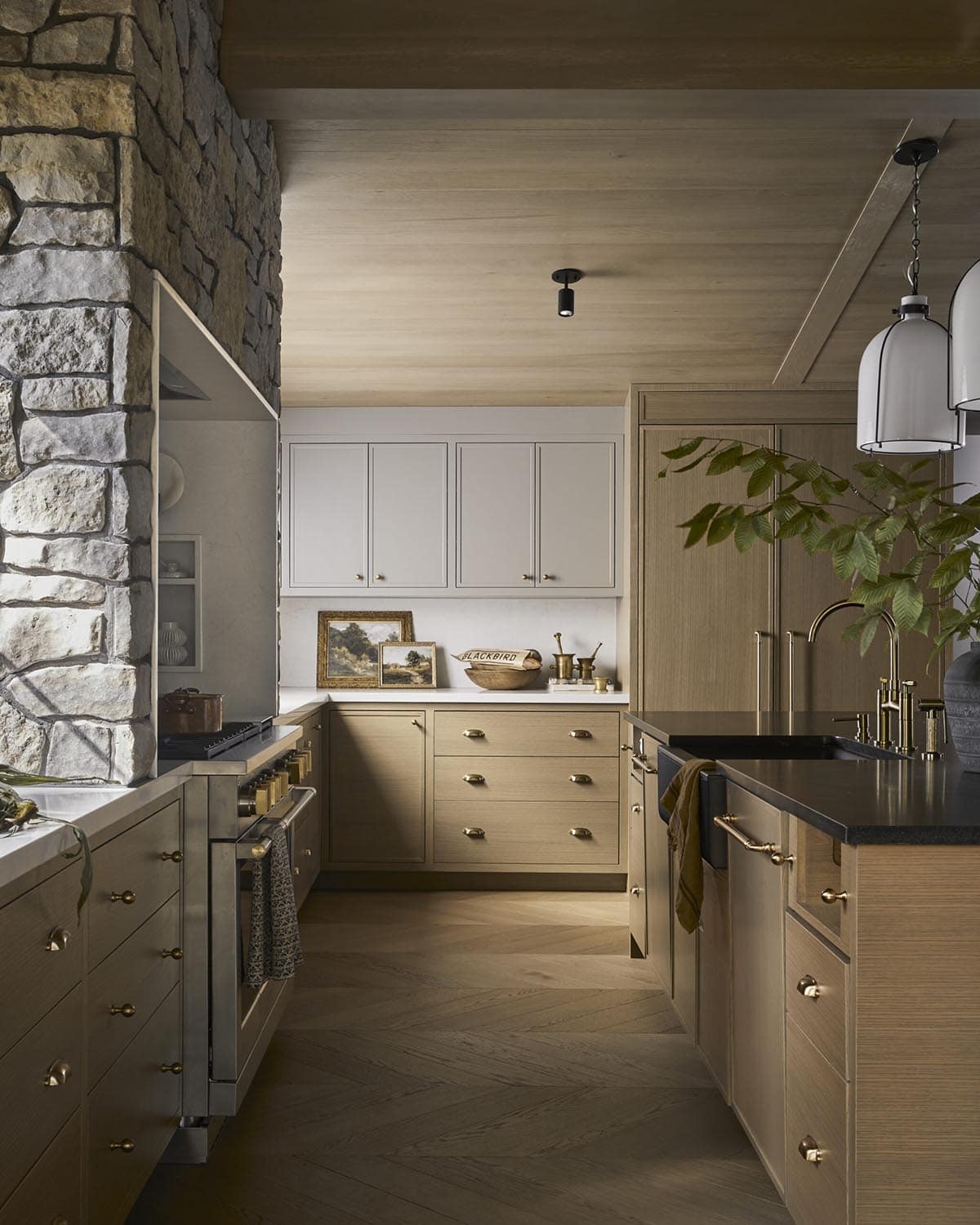 Kitchen view toward range and island with stone wall and wood cabinetry