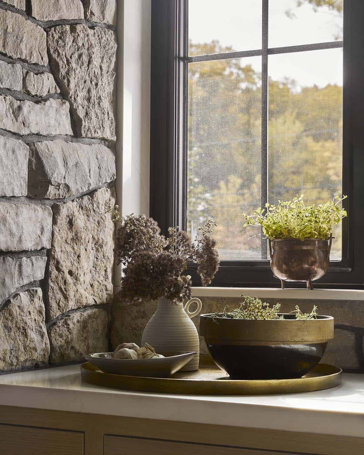 Kitchen windowsill with brass trays, dried flowers, and potted herbs