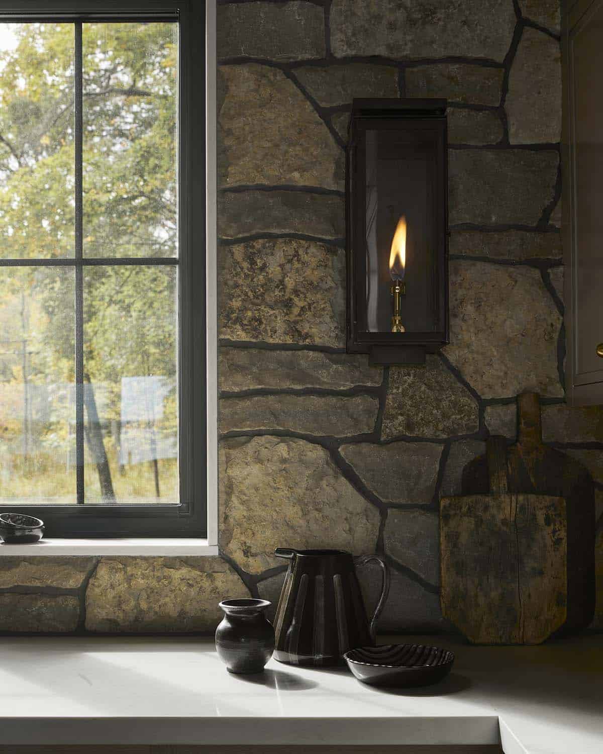 Stone kitchen wall with lit gas sconce and rustic cutting boards