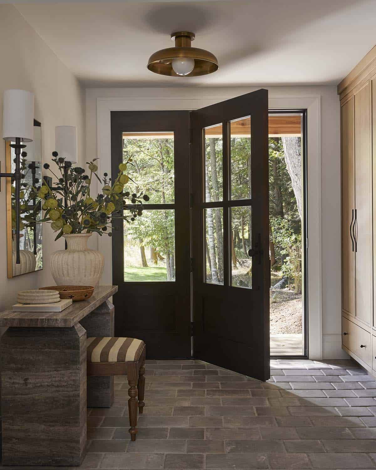 Entryway with dark front door open to wooded yard, stone floor, and console table